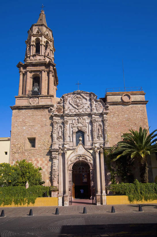 无人,教堂,竖图,室外,白天,仰视,旅游,度假,植物,标志建筑,道路,地标,建筑,路,棕榈树,叶子,墨西哥,阴影,节日,时间,光线,时钟,影子,小路,钟楼,绿叶,交通,计时,文化,娱乐,建设,树,树木,蓝色,绿色,蓝天,天空,阳光,自然,钟表,天,祈祷,享受,休闲,健康,嫩叶,表,旅游胜地,放松,许愿,宗教,信仰,生长,晴朗,成长,纪念,祈求,北美,北美洲,基督教,天主教,美洲,信念,棕榈叶,万里无云,阿瓜斯卡连特斯州,阿瓜斯卡连特斯,北亚美利加洲,亚美利加洲,塔钟,墨西哥合众国,仙人掌王国,平安,叶,叶片,钟,晴空,晴空万里,彩图,低角度拍摄,大教堂,礼拜堂